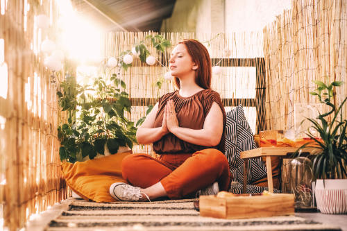 A woman in a bright wooden hut is meditating whilst looking peaceful.